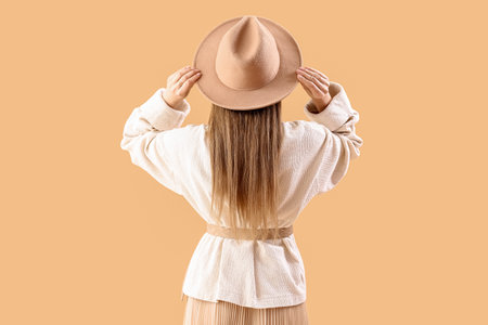 Beautiful fashionable young woman in hat and knitted sweater on beige background, back viewの写真素材