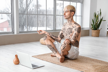 Young tattooed man meditating at homeの写真素材