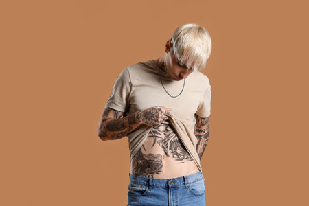 Young tattooed man in beige t-shirt on brown backgroundの写真素材