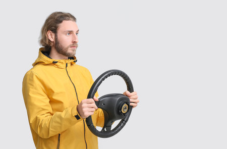 Handsome man with steering wheel on gray background
