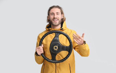 Handsome man with steering wheel on gray background