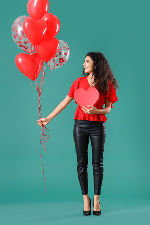 Beautiful young woman with gift and balloons on color background. Valentine's Day celebrationの写真素材