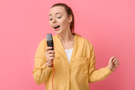Young woman with professional microphone singing on pink backgroundの写真素材