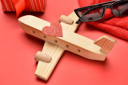 Wooden airplane with heart and sunglasses on red background, closeup. Valentine's Day celebrationの写真素材