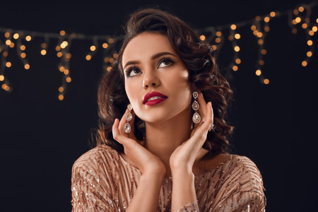 Portrait of beautiful woman touching earrings on dark backgroundの写真素材