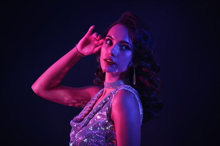Toned portrait of beautiful woman in shiny evening dress and stylish jewelry on dark backgroundの写真素材