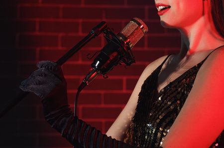 Woman with professional microphone singing on dark background, closeup