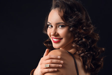 Portrait of young smiling woman touching her shoulder on dark background
