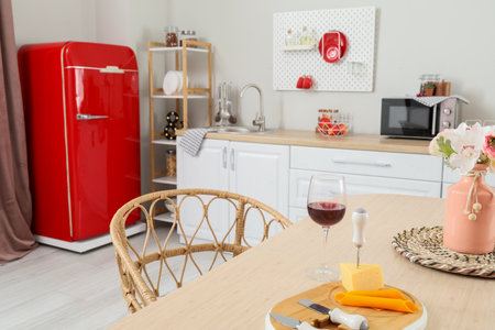 Vase with flowers, glass of wine and cheese board on dining table in kitchenの写真素材