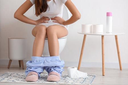 Young woman suffering from bellyache on toilet bowl in restroomの写真素材