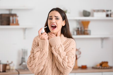 Young woman spraying her sore throat in kitchenの写真素材
