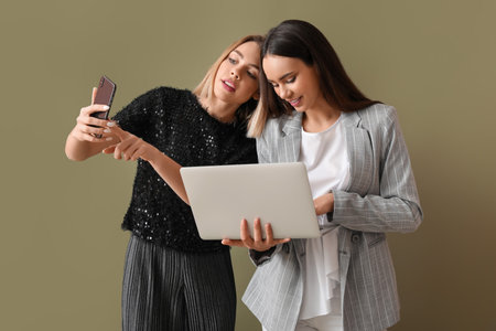 Young women with laptop and mobile phone on color backgroundの写真素材
