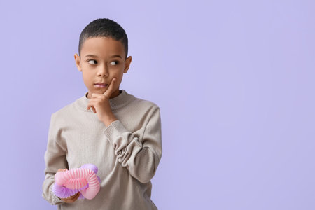 Thoughtful little African-American boy with pink Pop Tube on lilac backgroundの写真素材