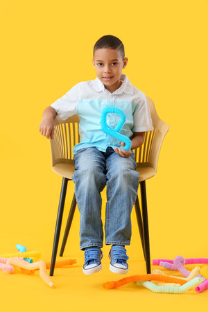 Little African-American boy with Pop Tubes sitting in chair on yellow backgroundの写真素材