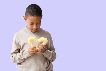 Little African-American boy with yellow Pop Tube on lilac backgroundの写真素材