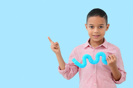 Little African-American boy with Pop Tube pointing at something on blue backgroundの写真素材
