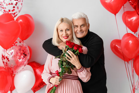 Happy mature couple with flowers and balloons on light background. Valentine's Day celebrationの写真素材