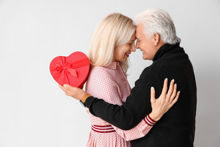 Happy mature couple with gift on light background. Valentine's Day celebrationの写真素材