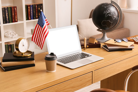 Laptop with blank screen and USA flag on desk in officeの写真素材