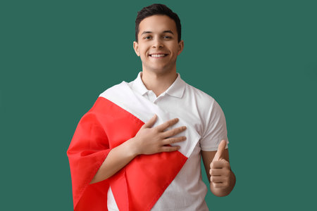Handsome young man with flag of Poland showing thumb-up on green backgroundの写真素材
