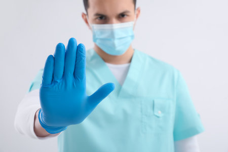 Male nurse in medical mask showing STOP gesture on light backgroundの写真素材