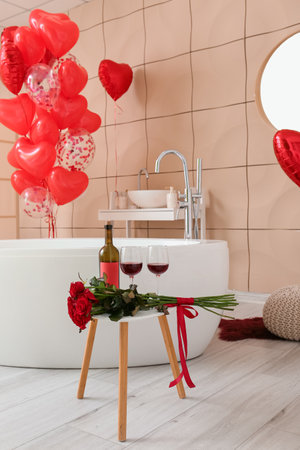 Glasses with wine, bottle and bouquet of flowers on table in bathroom decorated for Valentine's Dayの写真素材