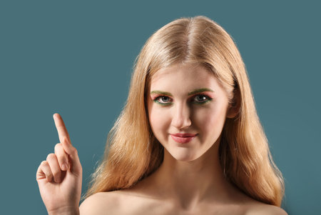 Beautiful girl with unusual eyebrows pointing at something on color backgroundの写真素材