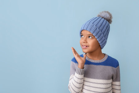 Cute little African-American boy in winter clothes looking away on color backgroundの写真素材