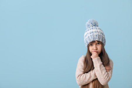 Sad little girl in winter clothes on color backgroundの写真素材