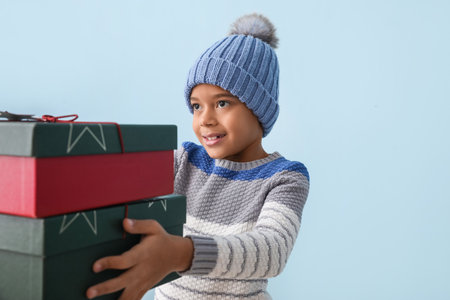 Cute little African-American boy in winter clothes and with Christmas gifts on color backgroundの写真素材