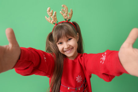 Cute little girl with reindeer horns taking selfie on color backgroundの写真素材