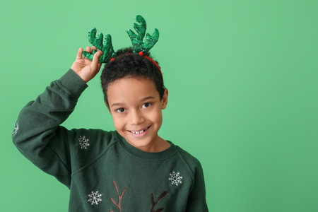 Cute little African-American boy with reindeer horns on color backgroundの写真素材