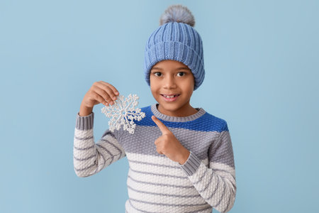 Cute little African-American boy in winter clothes and with snowflake on color backgroundの写真素材