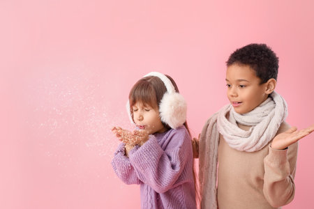 Cute little children in winter sweaters playing with snow on color backgroundの写真素材