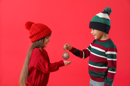 Cute little children in winter sweaters and with Christmas ball on color backgroundの写真素材