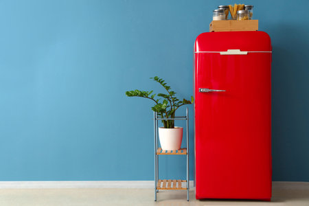 Red fridge with food, shelving unit and houseplant near blue wallの写真素材
