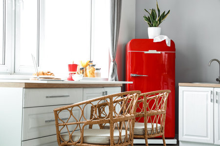 Interior of light modern kitchen with red fridge, white counters and wicker chairsの写真素材