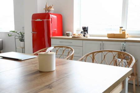 Dining table with tissue box and laptop in light kitchenの写真素材
