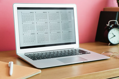 Laptop with digital calendar on desk near pink wall, closeupの写真素材