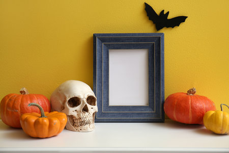 Blank frame with Halloween pumpkins and skull on mantelpiece near yellow wallの写真素材