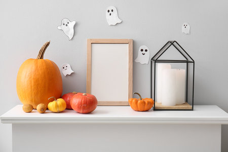 Blank frame with Halloween pumpkins and candles on mantelpiece near light wallの写真素材