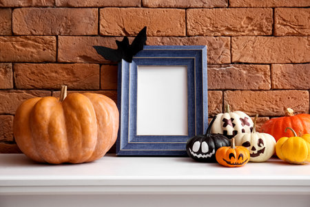 Blank frame with Halloween pumpkins on mantelpiece near brick wallの写真素材