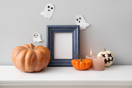 Blank frame with Halloween pumpkins and candles on mantelpiece near light wallの写真素材