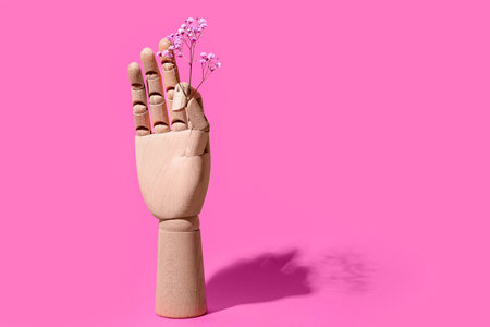Wooden hand with flowers on pink backgroundの写真素材