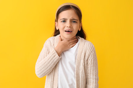 Little girl suffering from sore throat on yellow backgroundの写真素材