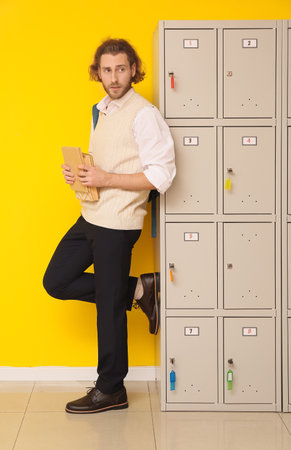 Male student with books near locker on yellow backgroundの写真素材
