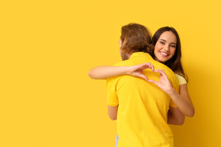 Hugging young couple in stylish t-shirts on yellow backgroundの写真素材