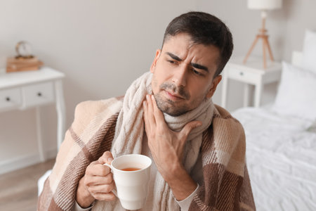 Ill young man with sore throat drinking hot tea at homeの写真素材