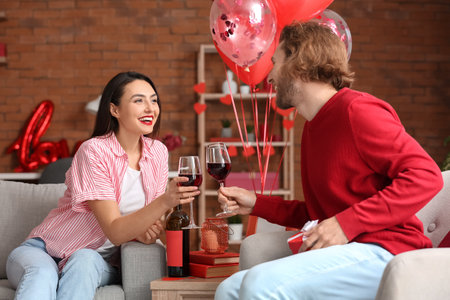 Happy young couple drinking wine at home on Valentine's Dayの写真素材