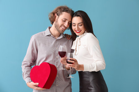 Happy young couple with gift and wine on color background. Valentine's Day celebration